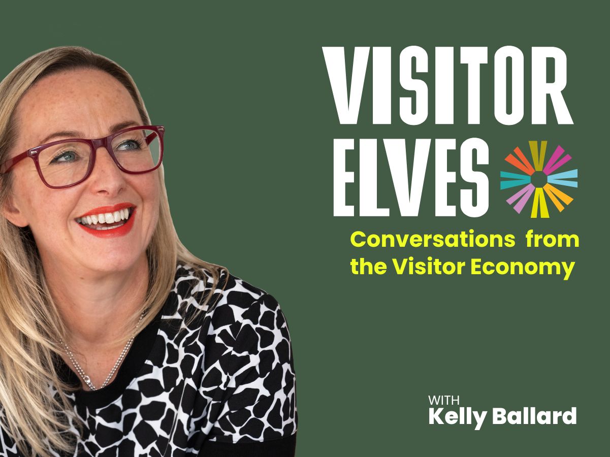 Happy Kelly holding a blue mug looking at the podcast name Elves of the Visitor economy